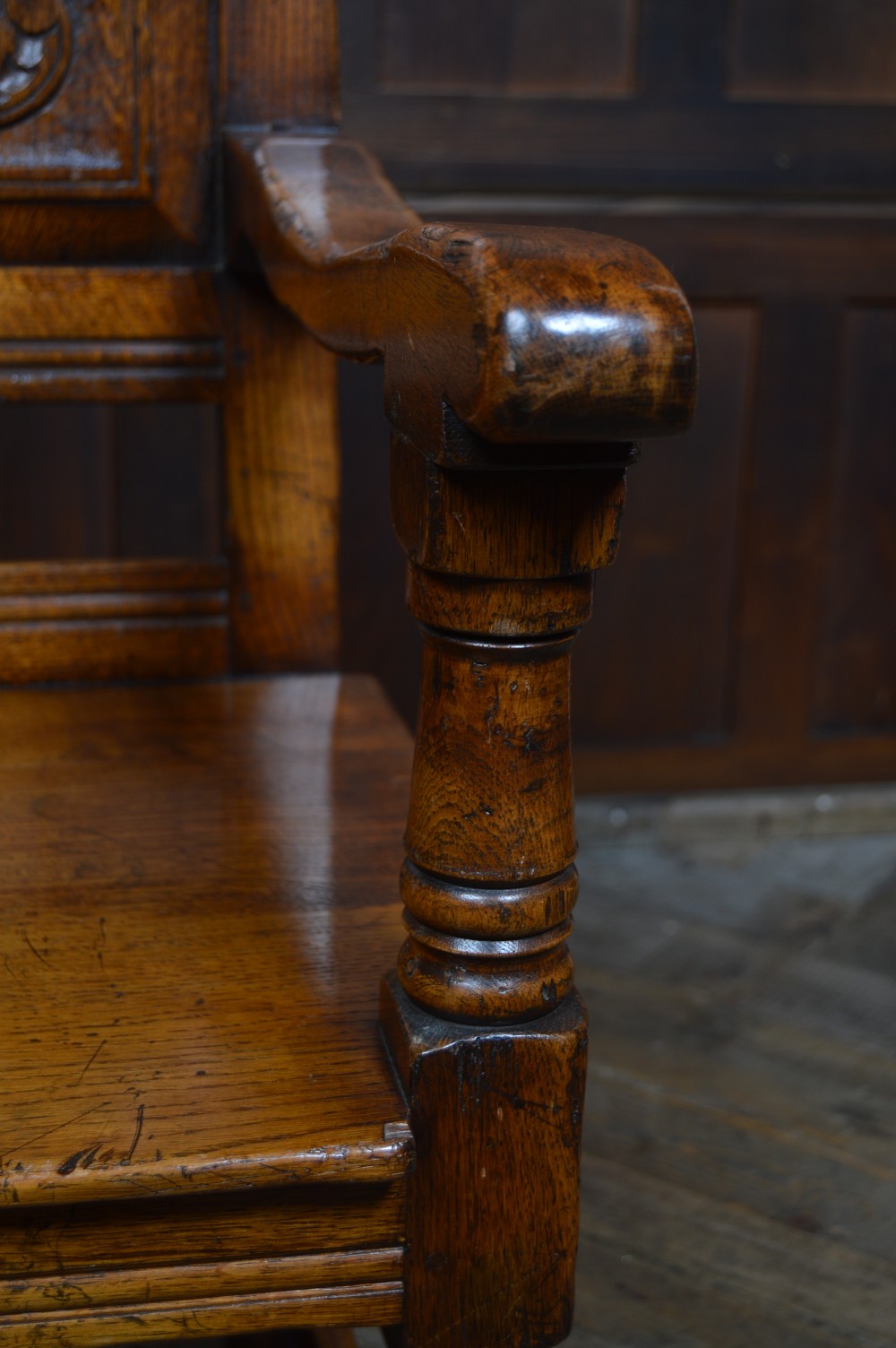 A carved dark oak wainscot style armchair featuring a floral relief panel back, shaped armrests, turned front legs, and wooden stretchers. View XI