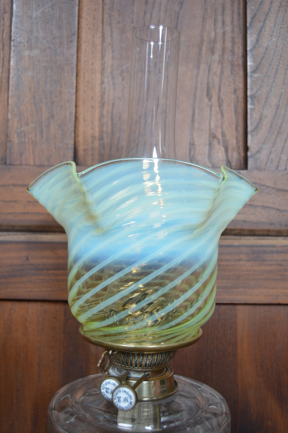 A Victorian brass oil lamp featuring a fluted column base, a clear glass reservoir, a light green swirl opalescent shade, and a tall glass chimney. View V