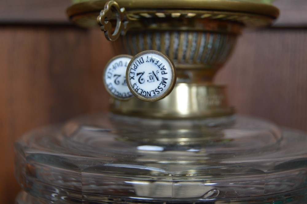 A Victorian brass oil lamp featuring a fluted column base, a clear glass reservoir, a light green swirl opalescent shade, and a tall glass chimney. View VI