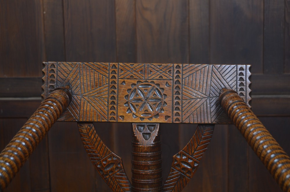 A carved oak Turners armchair featuring a triangular seat, three lathe-turned legs, bobbin-turned armrests, and geometric chip carving on the crest rail. View IV