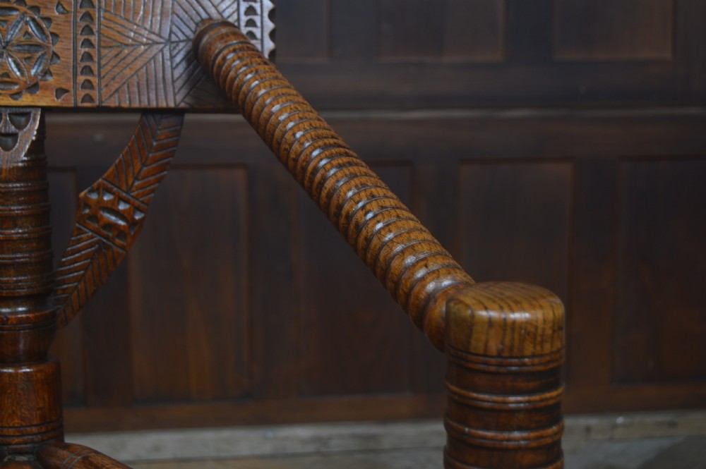 A carved oak Turners armchair featuring a triangular seat, three lathe-turned legs, bobbin-turned armrests, and geometric chip carving on the crest rail. View VI
