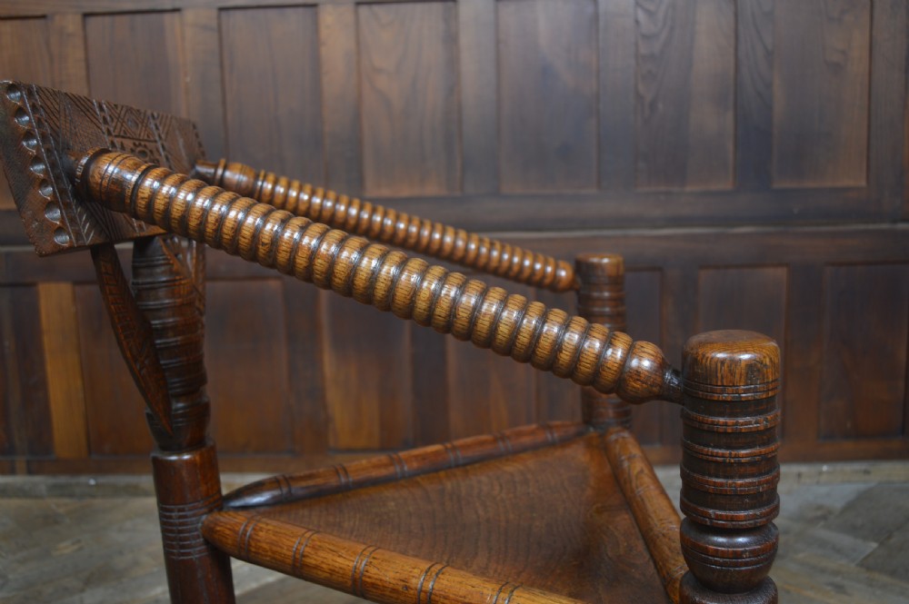 A carved oak Turners armchair featuring a triangular seat, three lathe-turned legs, bobbin-turned armrests, and geometric chip carving on the crest rail. View VIII