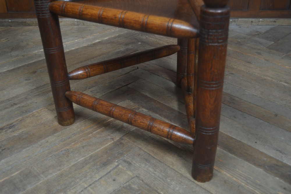 A carved oak Turners armchair featuring a triangular seat, three lathe-turned legs, bobbin-turned armrests, and geometric chip carving on the crest rail. View IX