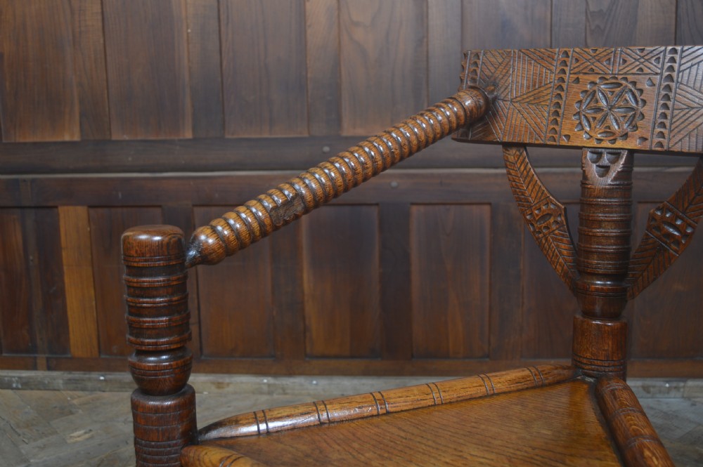 A carved oak Turners armchair featuring a triangular seat, three lathe-turned legs, bobbin-turned armrests, and geometric chip carving on the crest rail. View XV