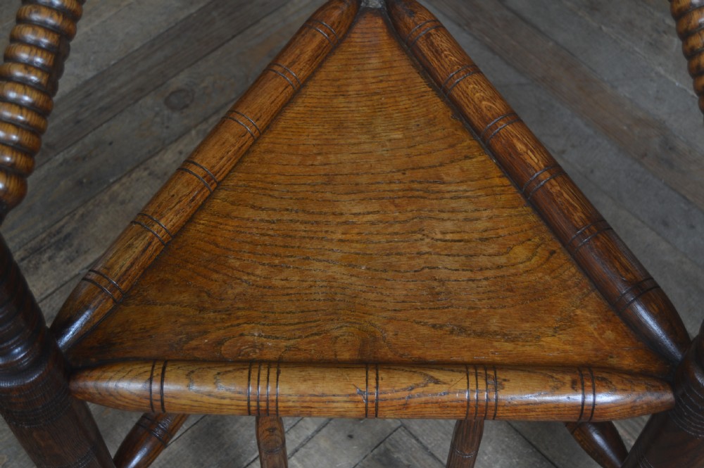 A carved oak Turners armchair featuring a triangular seat, three lathe-turned legs, bobbin-turned armrests, and geometric chip carving on the crest rail. View XVI