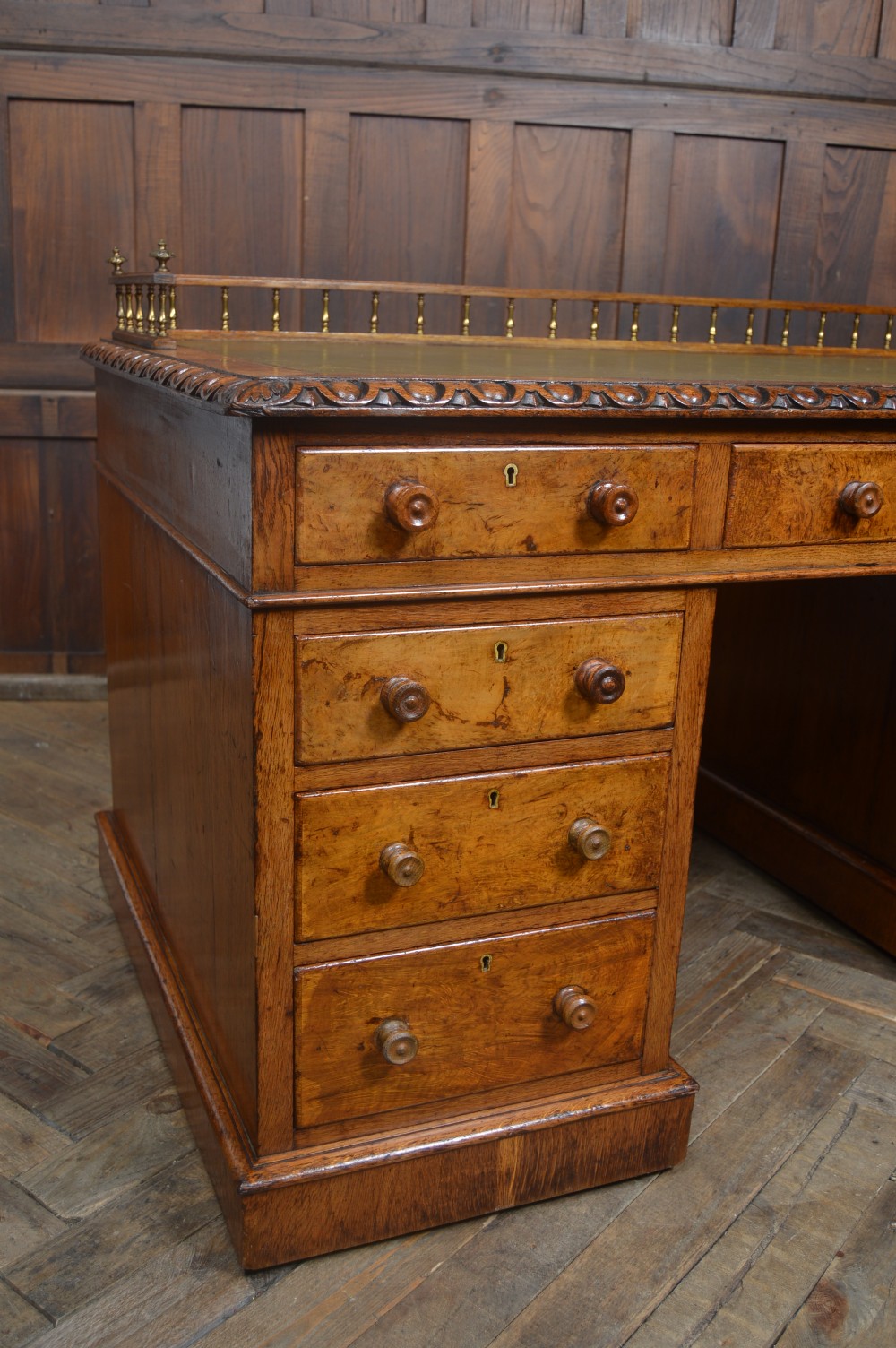 Victorian warm brown oak pedestal writing desk with a green leather inset top, brass gallery rail, and nine drawers. View II