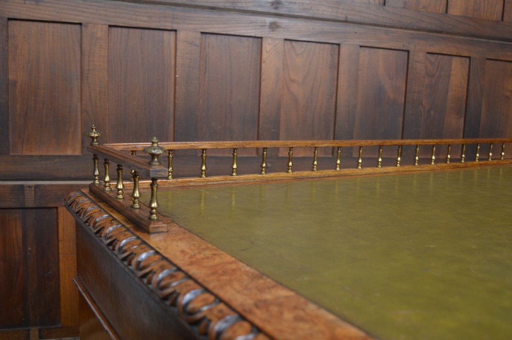 Victorian warm brown oak pedestal writing desk with a green leather inset top, brass gallery rail, and nine drawers. View V