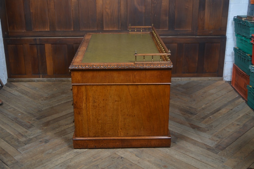 Victorian warm brown oak pedestal writing desk with a green leather inset top, brass gallery rail, and nine drawers. View XI