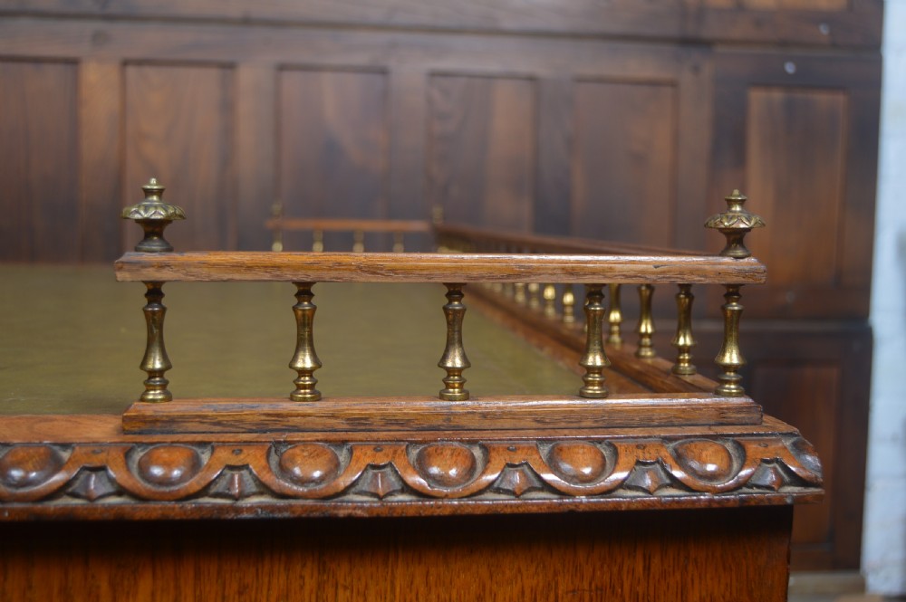 Victorian warm brown oak pedestal writing desk with a green leather inset top, brass gallery rail, and nine drawers. View XII
