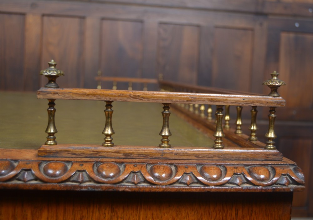 Victorian warm brown oak pedestal writing desk with a green leather inset top, brass gallery rail, and nine drawers. View XVI