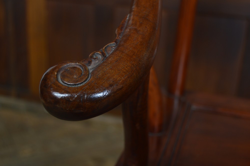 A Chinese carved wooden armchair featuring a continuous curved horseshoe backrail, carved central splat with a figurative relief, and a dark warm brown lacquered finish. View V