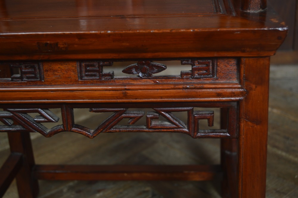 A Chinese carved wooden armchair featuring a continuous curved horseshoe backrail, carved central splat with a figurative relief, and a dark warm brown lacquered finish. View VI