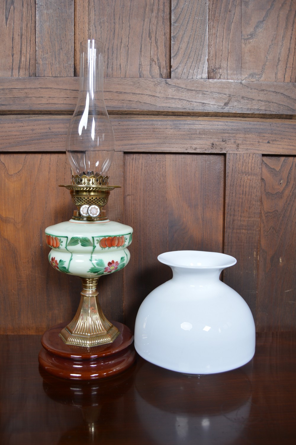 An antique Victorian paraffin oil lamp featuring a hand-painted floral glass reservoir, a brass fluted stem, a white opaline shade, and a circular wooden plinth base. View VIII