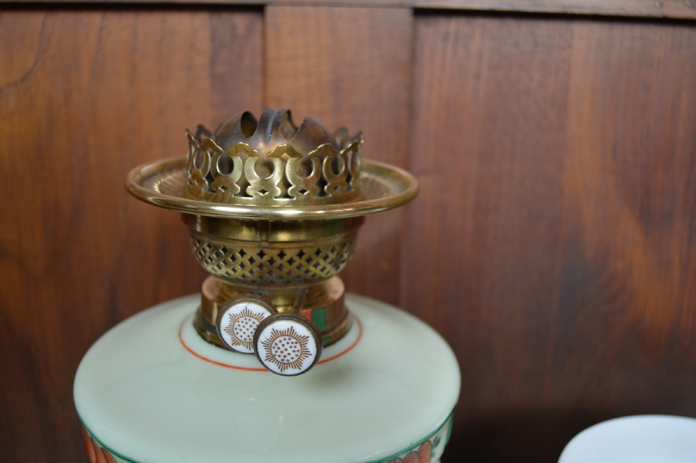 An antique Victorian paraffin oil lamp featuring a hand-painted floral glass reservoir, a brass fluted stem, a white opaline shade, and a circular wooden plinth base. View XI