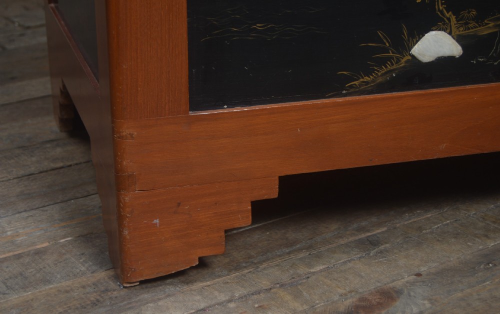 A Chinese camphor wood storage chest featuring a reddish-brown frame, black lacquer panels with figurative inlays, and a brass front clasp. View III