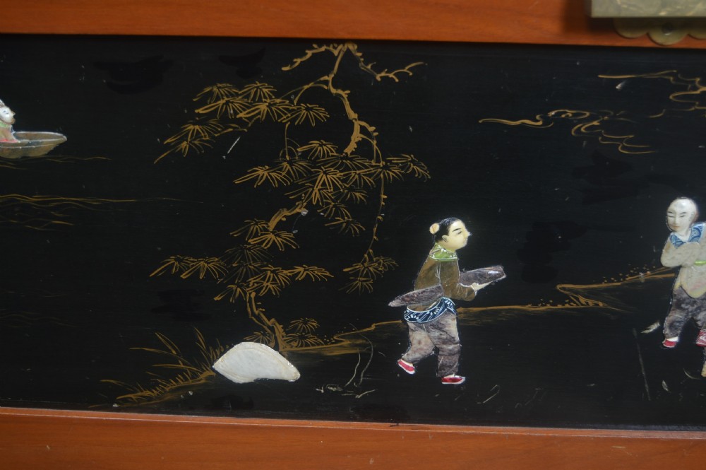 A Chinese camphor wood storage chest featuring a reddish-brown frame, black lacquer panels with figurative inlays, and a brass front clasp. View VI