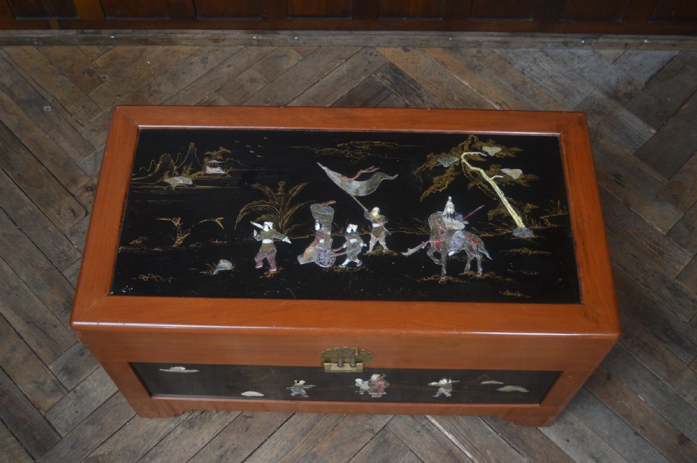 A Chinese camphor wood storage chest featuring a reddish-brown frame, black lacquer panels with figurative inlays, and a brass front clasp. View VII