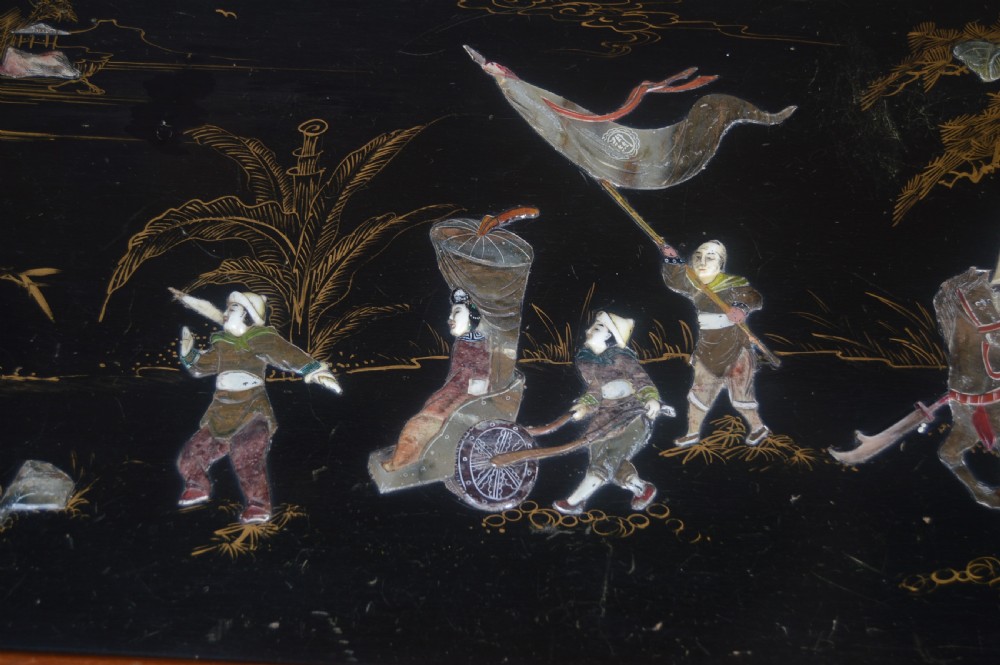 A Chinese camphor wood storage chest featuring a reddish-brown frame, black lacquer panels with figurative inlays, and a brass front clasp. View IX