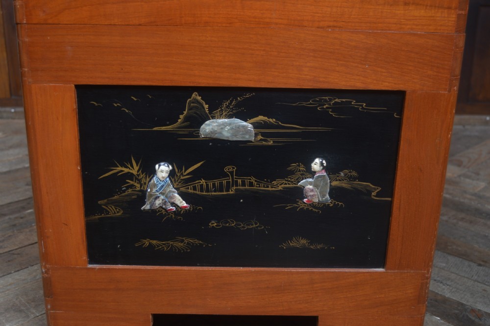 A Chinese camphor wood storage chest featuring a reddish-brown frame, black lacquer panels with figurative inlays, and a brass front clasp. View XIV