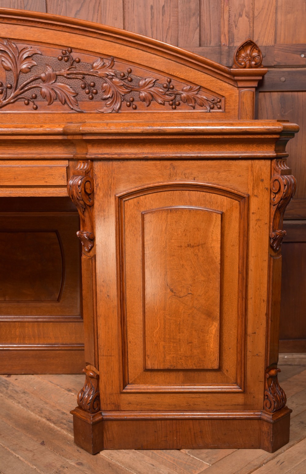 A Victorian oak pedestal sideboard featuring an arched carved backboard with foliage details, twin cupboard pedestals, and a recessed central section. View VII