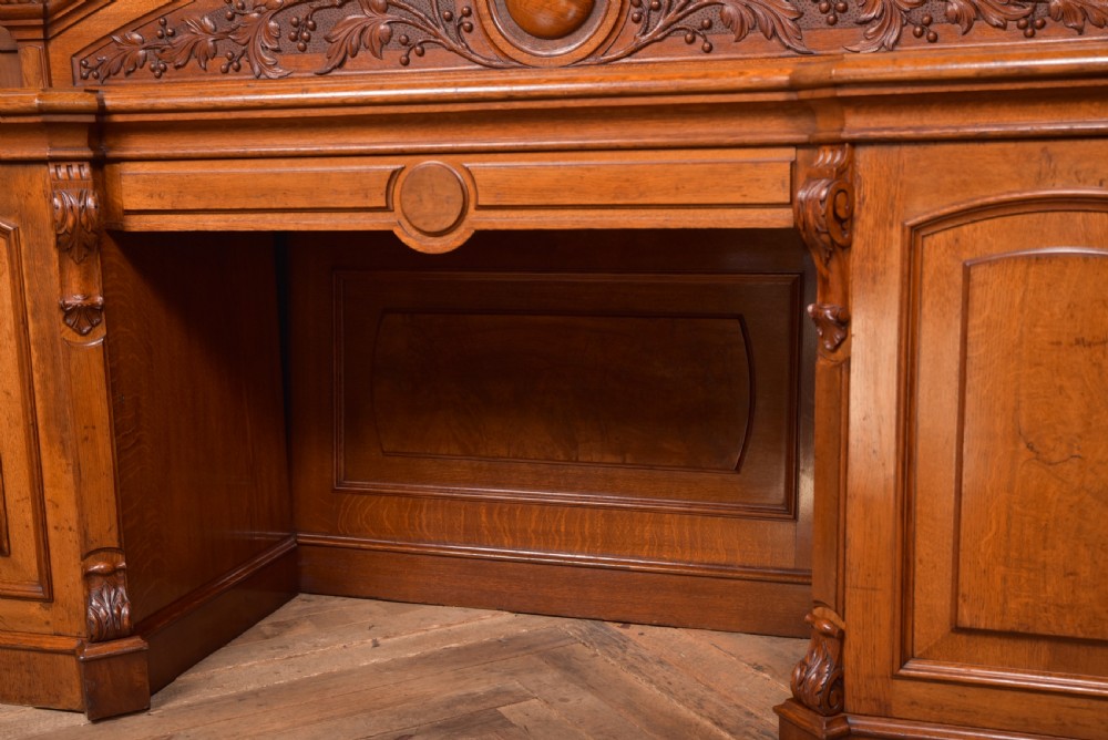 A Victorian oak pedestal sideboard featuring an arched carved backboard with foliage details, twin cupboard pedestals, and a recessed central section. View VIII