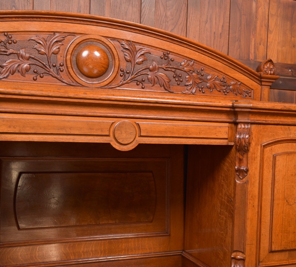 A Victorian oak pedestal sideboard featuring an arched carved backboard with foliage details, twin cupboard pedestals, and a recessed central section. View X