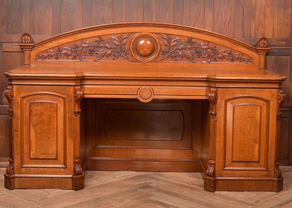 A Victorian oak pedestal sideboard featuring an arched carved backboard with foliage details, twin cupboard pedestals, and a recessed central section. View XI