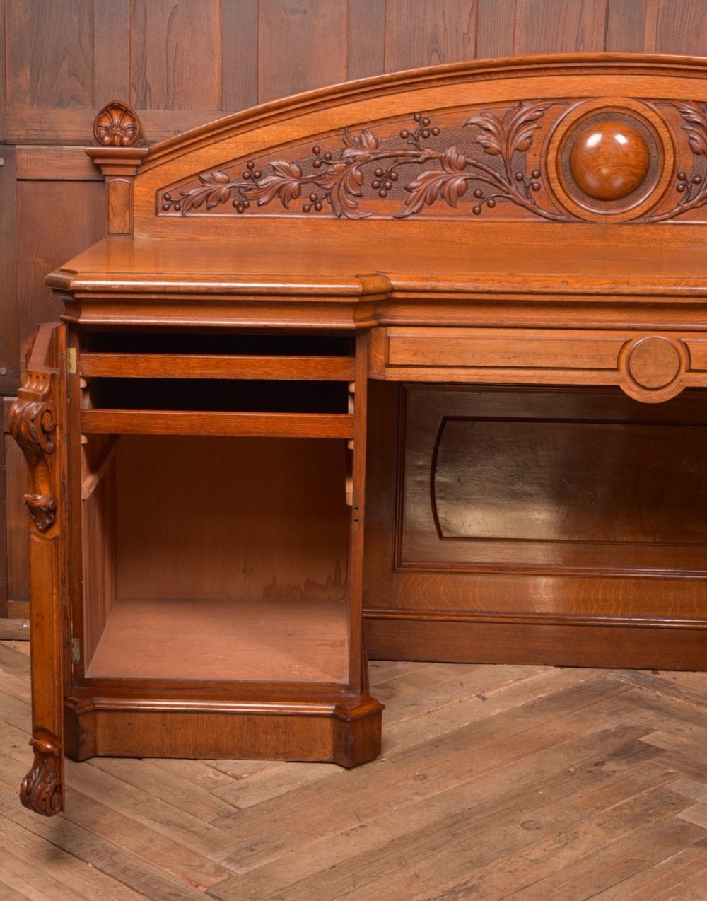 A Victorian oak pedestal sideboard featuring an arched carved backboard with foliage details, twin cupboard pedestals, and a recessed central section. View XII