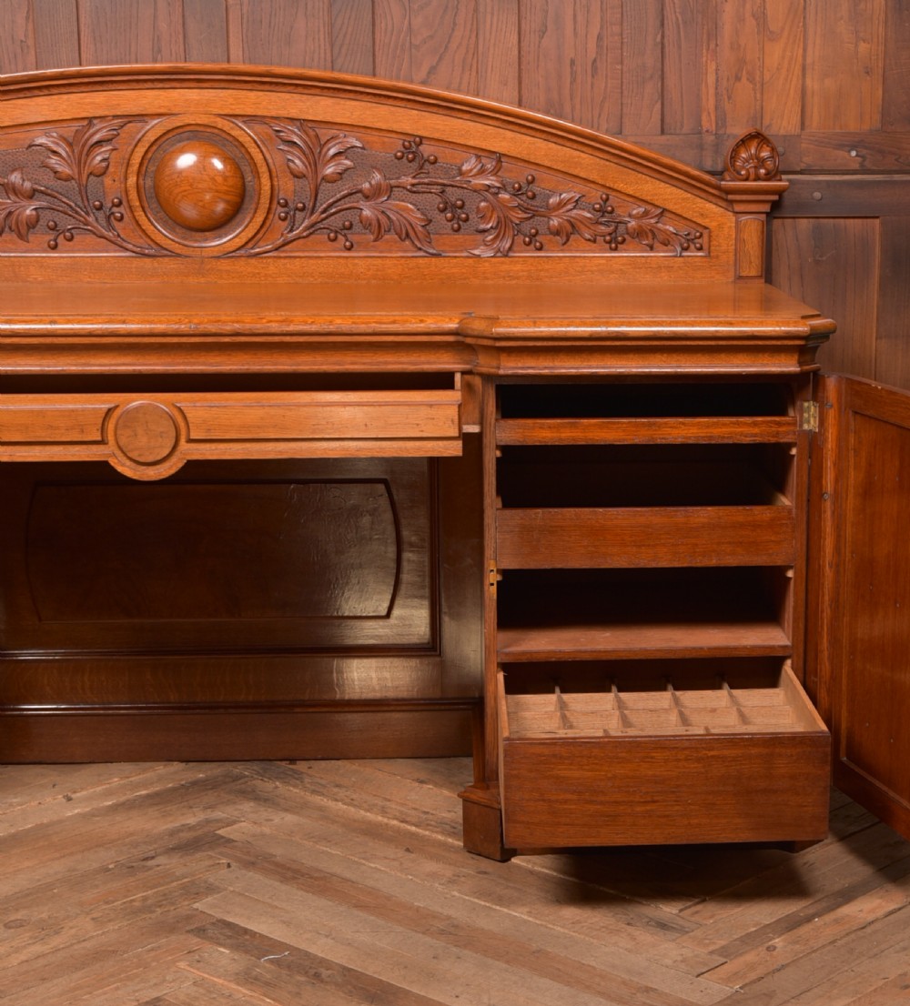 A Victorian oak pedestal sideboard featuring an arched carved backboard with foliage details, twin cupboard pedestals, and a recessed central section. View XIII