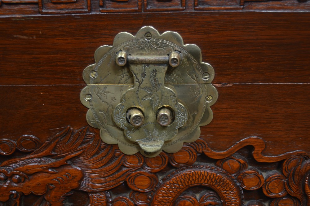 A carved warm brown camphor wood chest featuring a relief dragon motif on the front panel and a decorative circular brass clasp. View VII