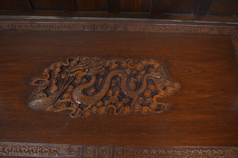 A carved warm brown camphor wood chest featuring a relief dragon motif on the front panel and a decorative circular brass clasp. View VIII