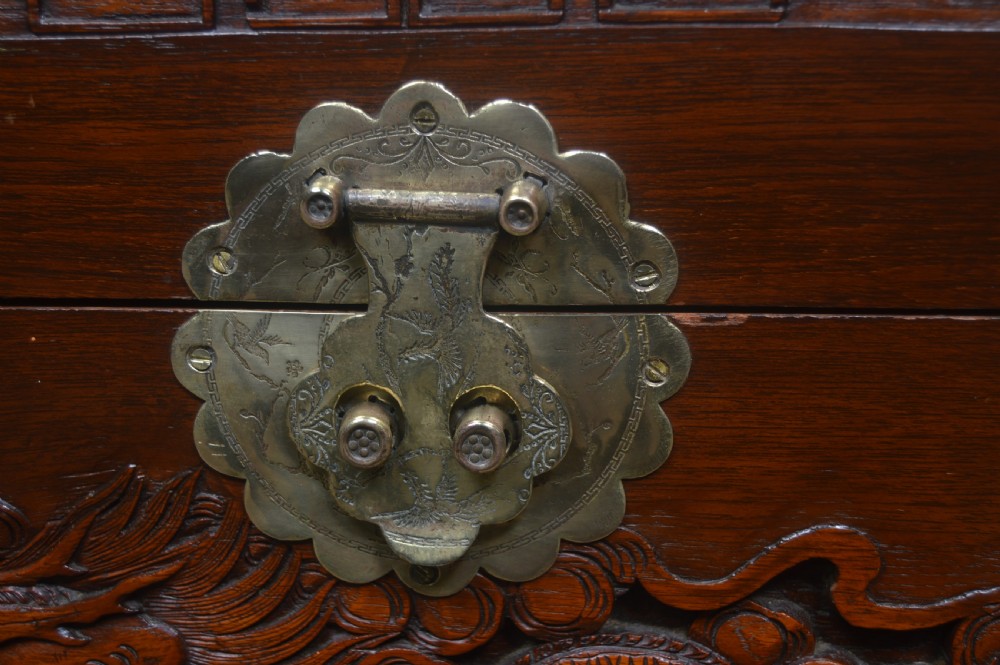 A carved warm brown camphor wood chest featuring a relief dragon motif on the front panel and a decorative circular brass clasp. View XVIII