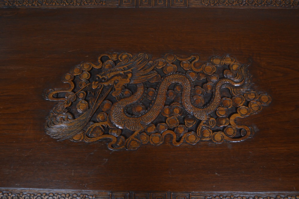 A carved warm brown camphor wood chest featuring a relief dragon motif on the front panel and a decorative circular brass clasp. View XXII