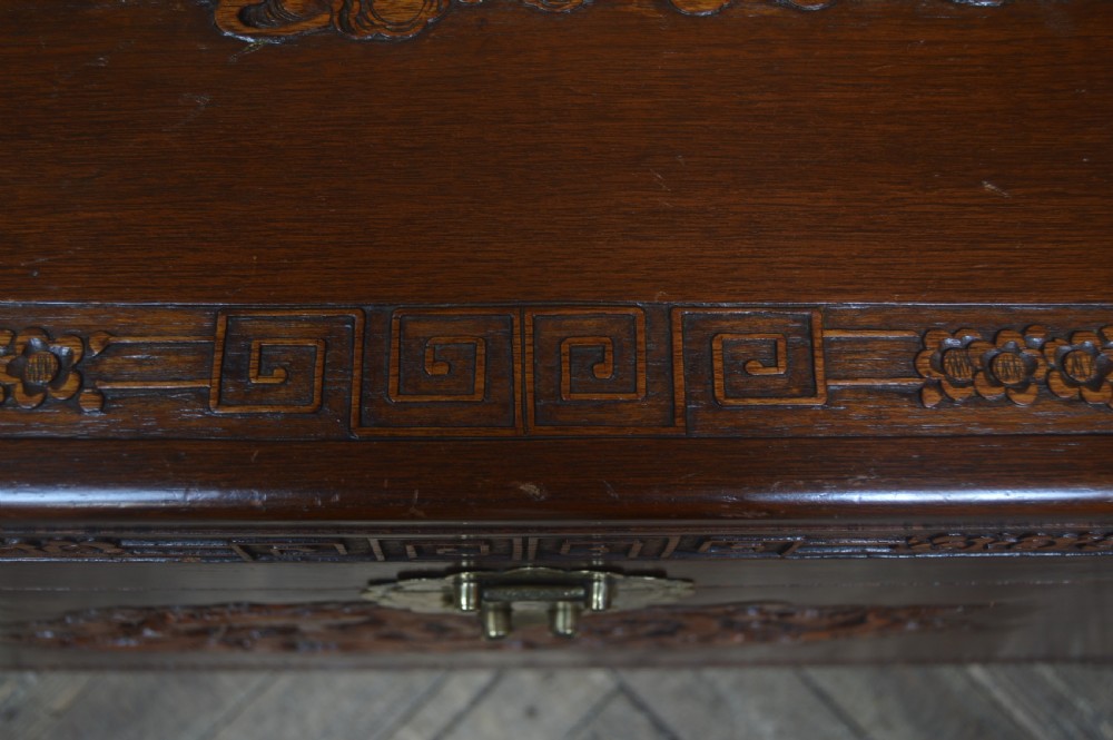 A carved warm brown camphor wood chest featuring a relief dragon motif on the front panel and a decorative circular brass clasp. View XXIII