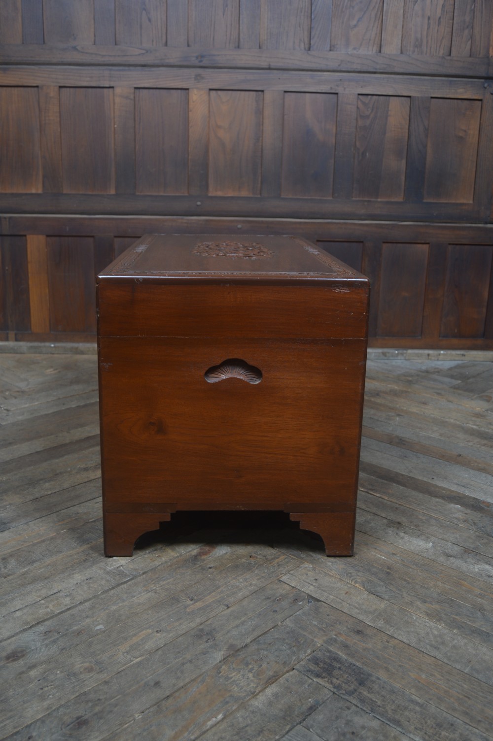 A carved warm brown camphor wood chest featuring a relief dragon motif on the front panel and a decorative circular brass clasp. View XXVII