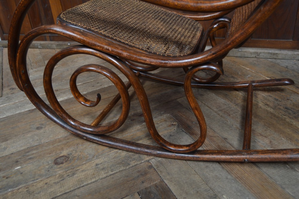 An Edwardian dark brown bentwood rocking chair featuring side scrollwork and woven cane panels on the seat and backrest. View VI