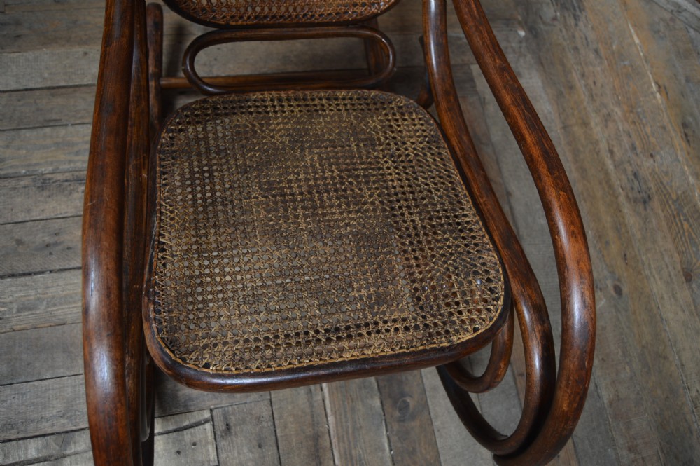 An Edwardian dark brown bentwood rocking chair featuring side scrollwork and woven cane panels on the seat and backrest. View VIII