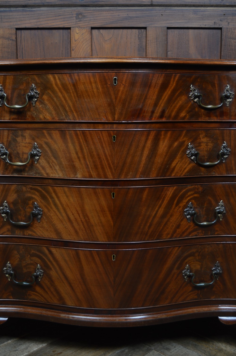 An 18th-century Georgian flame mahogany serpentine chest of drawers featuring four graduated drawers with rococo brass handles and ogee bracket feet. View V