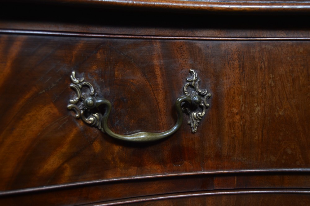 An 18th-century Georgian flame mahogany serpentine chest of drawers featuring four graduated drawers with rococo brass handles and ogee bracket feet. View VI