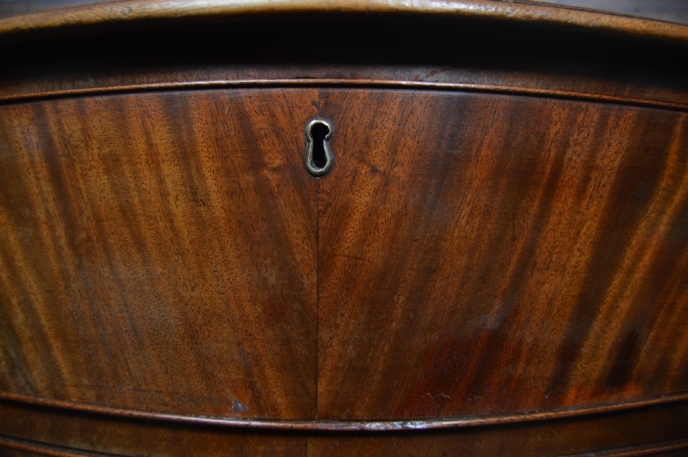 An 18th-century Georgian flame mahogany serpentine chest of drawers featuring four graduated drawers with rococo brass handles and ogee bracket feet. View VII