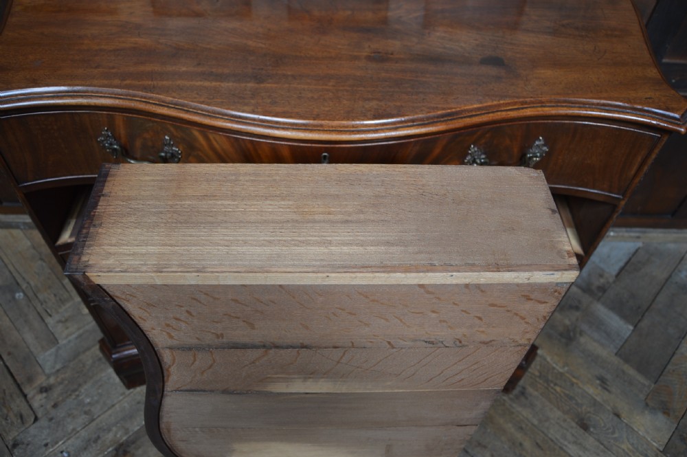 An 18th-century Georgian flame mahogany serpentine chest of drawers featuring four graduated drawers with rococo brass handles and ogee bracket feet. View XI