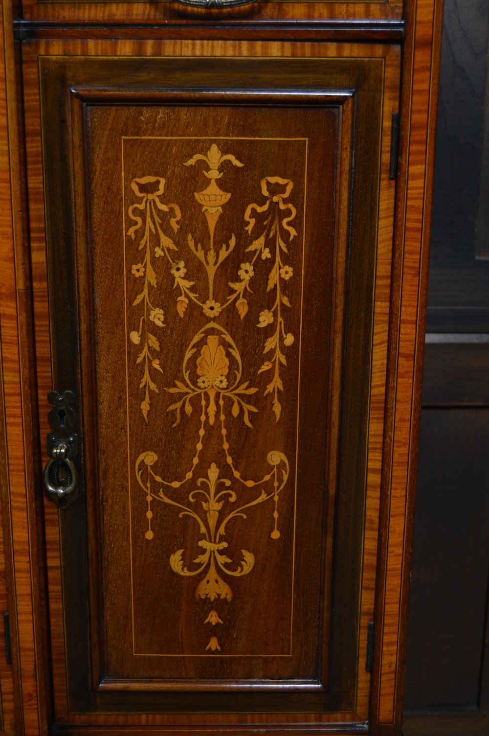 An Edwardian mahogany display cabinet featuring floral marquetry inlay, an oval mirror backdrop, astragal glazed central door, and slender cabriole legs. View III