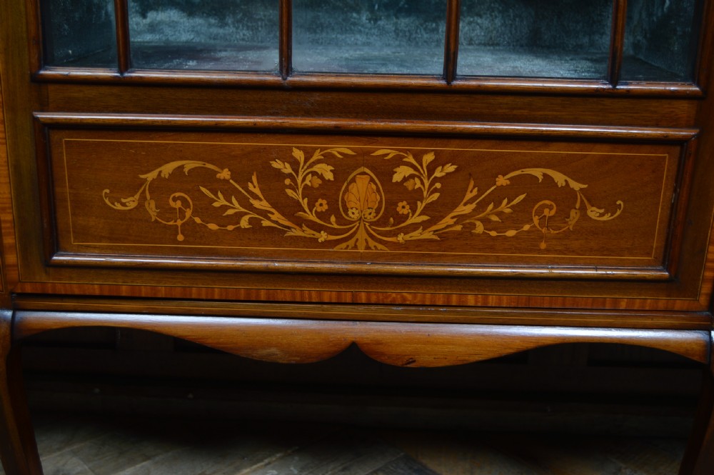 An Edwardian mahogany display cabinet featuring floral marquetry inlay, an oval mirror backdrop, astragal glazed central door, and slender cabriole legs. View V