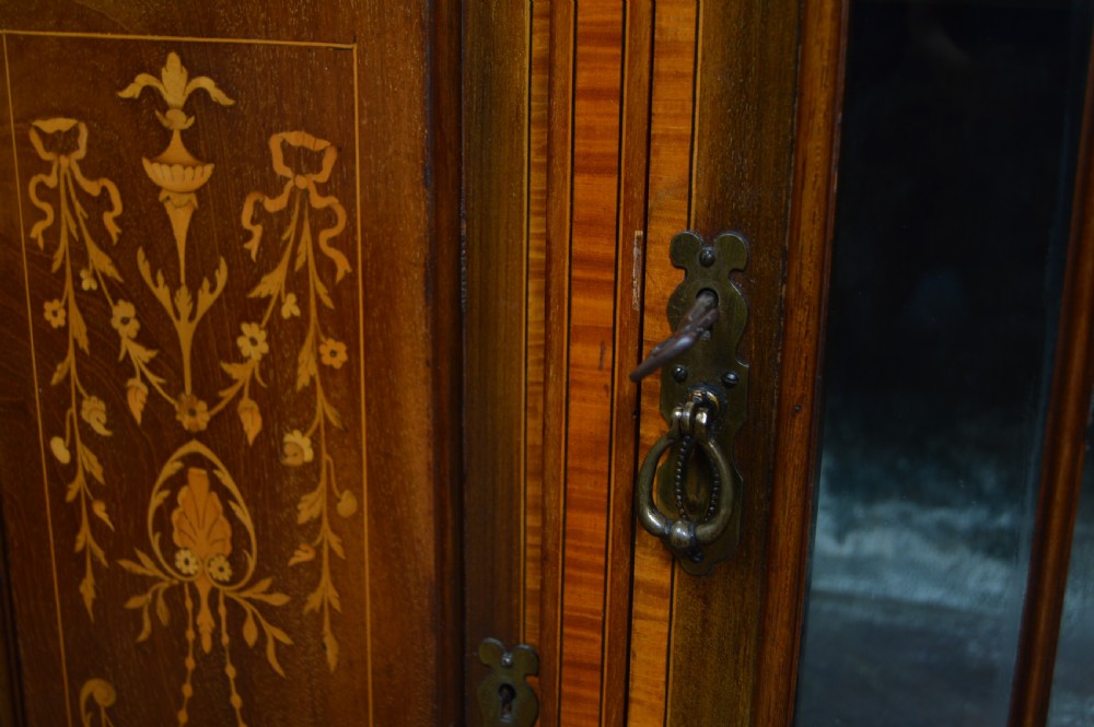 An Edwardian mahogany display cabinet featuring floral marquetry inlay, an oval mirror backdrop, astragal glazed central door, and slender cabriole legs. View VI
