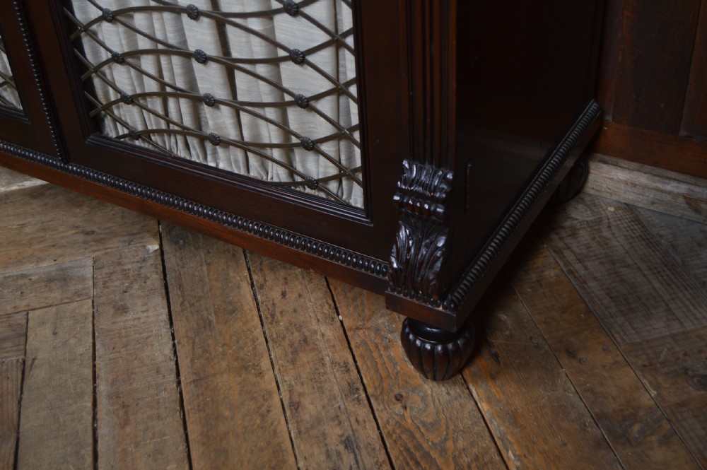 An antique dark mahogany chiffonier featuring a mirrored back shelf with a brass gallery, curved scroll supports, and lower cupboard doors with wire mesh and pleated fabric panels. View XI
