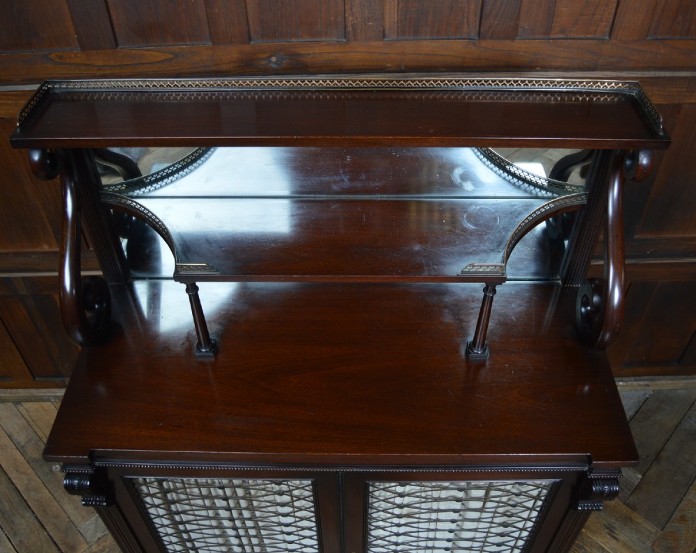An antique dark mahogany chiffonier featuring a mirrored back shelf with a brass gallery, curved scroll supports, and lower cupboard doors with wire mesh and pleated fabric panels. View XXIII