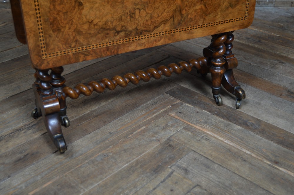 A Victorian burr walnut Sutherland drop-leaf table featuring inlaid geometric borders and barley twist legs on brass castors. View VI