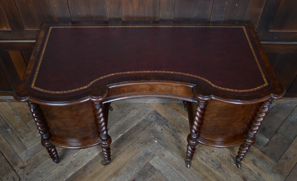 A Victorian kidney-shaped mahogany writing desk featuring a gilt-tooled maroon leather inset top and four barley twist legs on brass castors. View III