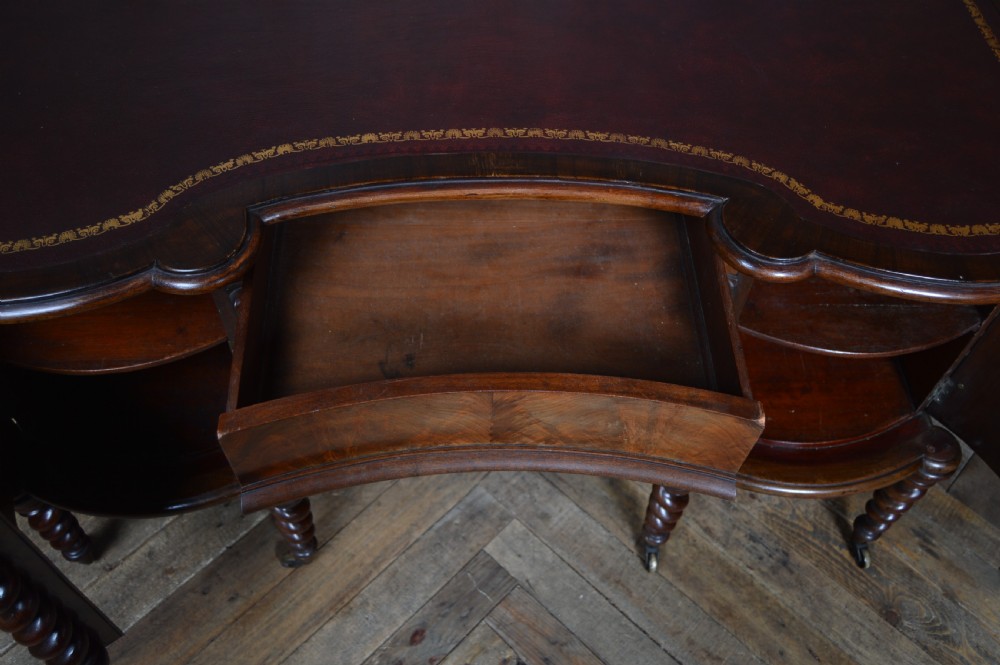 A Victorian kidney-shaped mahogany writing desk featuring a gilt-tooled maroon leather inset top and four barley twist legs on brass castors. View XI