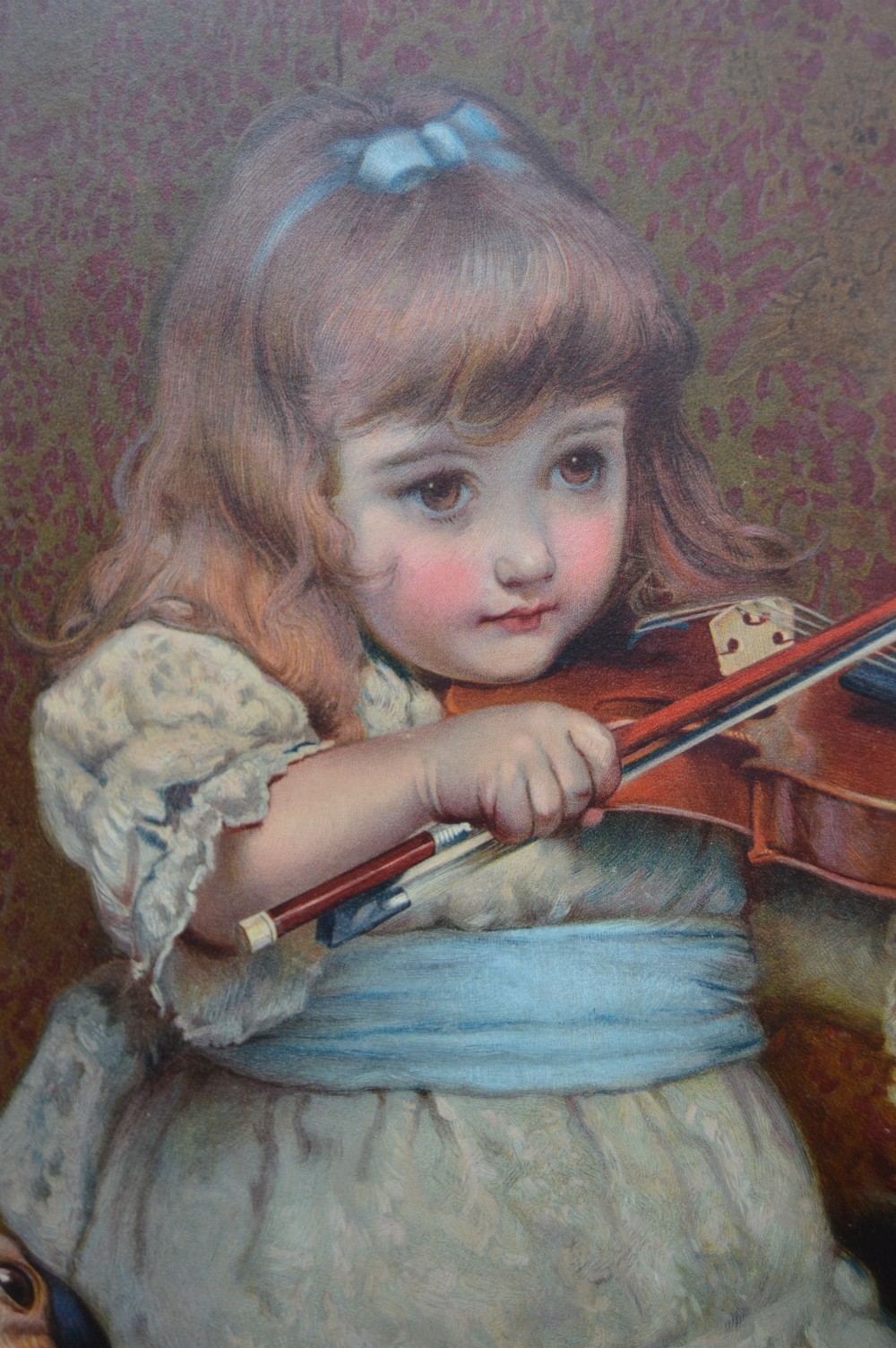 A framed Victorian chromolithograph after Charles Burton Barber depicting a young girl playing a violin to a terrier and kitten, set within a carved dark wood frame. View VII